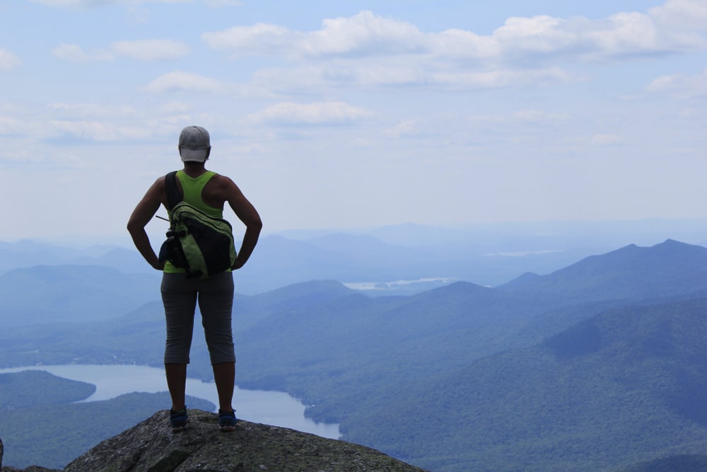 Things to do in the Adirondacks, photo of a person on top of a mountain looking out over the Adirondacks
