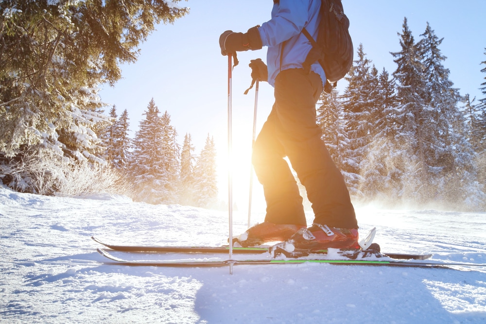 Skiier on white snow, trees and sun flare in background at Gore Mountain Ski Resort.